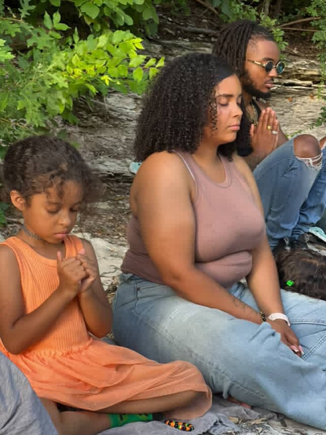 Three people in meditation outdoors during a community wellness gathering